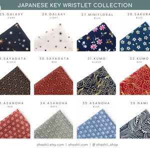 May include: A collection of 12 Japanese key wristlets featuring different patterns and colors. The wristlets are made of fabric and have a variety of designs, including stars, flowers, clouds, and geometric shapes. The wristlets are labeled with numbers and names, such as "Galaxy Dark", "Minifloral Blue", and "Sayagata Black".