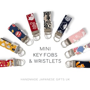 Puede incluir: Una colección de mini llaveros y pulseras con diseños japoneses. Los llaveros presentan patrones como gatos, flores y formas geométricas. Cada uno tiene un anillo de metal. El texto dice "MINI KEY FOBS & WRISTLETS" y "HANDMADE JAPANESE GIFTS UK".