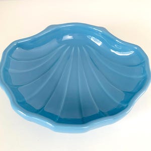 May include: A light blue, seashell-shaped dish. The dish has a glossy finish and a scalloped edge. The interior features a fan-like pattern. This decorative dish is ideal for serving snacks or as a decorative accent.