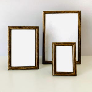 May include: Three rectangular picture frames with a dark brown wood grain finish and white matting. The frames are arranged in a group, featuring one large vertical frame and two smaller vertical frames of varying sizes, all with clean edges.