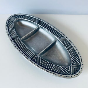 May include: A silver oval serving dish with three divided sections. The dish has a decorative border with a geometric pattern.