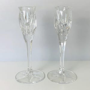 May include: Two clear glass candle holders with a tall, slender design. The candle holders have a textured, swirling pattern on the upper portion and a round base. The overall aesthetic is elegant and suitable for home decor.