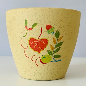 May include: A yellow ceramic planter with a speckled finish. The planter has a floral design with red, orange, green, and blue leaves and a yellow acorn.
