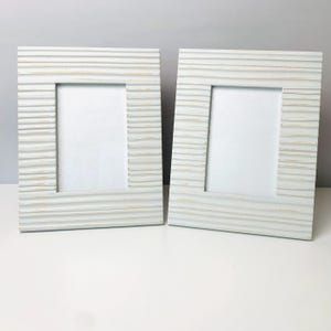 May include: Two matching rectangular picture frames. The frames are painted a light blue with a textured, horizontal, ridged design. The inner portion of the frames are white, ready for a photo. The frames are displayed on a white surface.
