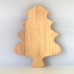 May include: A light brown wooden serving board shaped like a Christmas tree. The board features a smooth surface with visible natural wood grain patterns, a pointed top, tiered branches, and a rectangular base at the bottom of the tree shape.