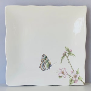 May include: White square ceramic plate with a green and orange butterfly and pink flowers on a branch.