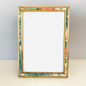 May include: A rectangular picture frame featuring a thin, metallic gold border with a beaded texture. The frame is decorated with a colorful floral pattern in shades of pink, blue, green, and yellow, surrounding a blank, white rectangular center.