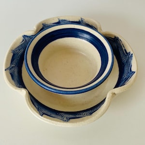 May include: A set of two ceramic bowls with a white base and blue stripes. The smaller bowl is nested inside the larger bowl, which has a wavy edge.
