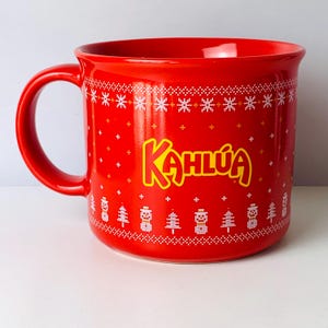 May include: A red ceramic mug with a handle, featuring the word "Kahlúa" in yellow script. The mug is decorated with white snowflake and Christmas tree patterns, perfect for holiday beverages.