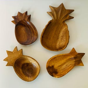 May include: Four wooden pineapple-shaped bowls. The bowls are made of dark brown wood and have a natural, rustic finish. They are perfect for serving snacks, dips, or small dishes.