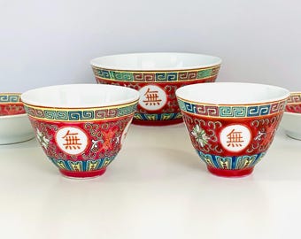 May include: A set of ceramic bowls featuring a vibrant red background with intricate floral patterns, blue and yellow geometric borders, and a central white circular medallion containing the black Chinese character for nothing, 無.