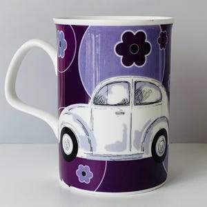 May include: White ceramic mug with a purple and lavender floral design and a white car illustration. The mug has a white handle and is decorated with purple flowers and circles. The car is white with black tires.