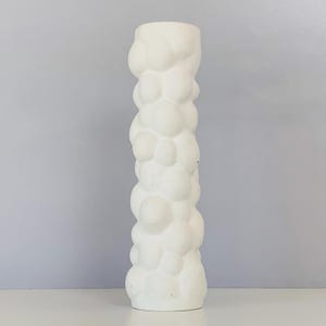 May include: White ceramic vase with a textured, bubble-like design. The vase is tall and slender, with a rounded base.
