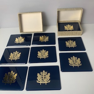May include: Set of eight blue coasters with gold royal crests. The coasters are in a box with a beige and brown woven pattern.