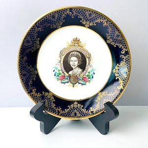 May include: A decorative plate featuring a portrait of Queen Elizabeth II, with the text "Silver Jubilee 1952-1977." The plate has a navy blue border with gold filigree and a gold rim. The center of the plate is white.
