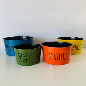 May include: Four colorful ceramic bowls with black lettering. The bowls are labeled "Potato", "Mixed Nuts", "Candies", and "Pretzels".