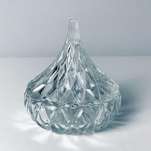May include: Clear glass candy dish with a diamond pattern and a pointed lid. The dish is round at the base and tapers to a point at the top. The lid has a textured, ridged design. The dish is empty and sits on a white surface.