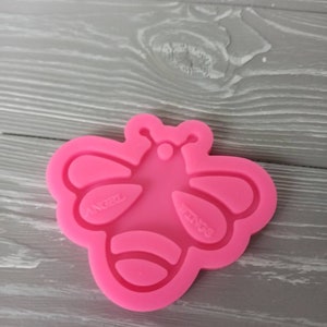 May include: Pink silicone mold shaped like a bee with the words "Angel Wings" on the wings.