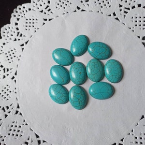 May include: A collection of ten oval-shaped turquoise cabochons, each with a unique pattern of veining. The stones are arranged on a white doily.