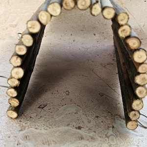 Pode incluir: Uma pequena ponte arqueada construída a partir de numerosos pequenos troncos de madeira natural. Os troncos estão dispostos em forma curva, criando uma estrutura semelhante a um túnel. As extremidades dos troncos são visíveis, mostrando o grão natural da madeira. Este item é provavelmente para animais de estimação pequenos.
