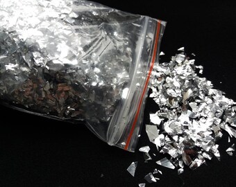 May include: A plastic bag filled with silver glitter confetti. The bag is open and the confetti is spilling out onto a black surface.