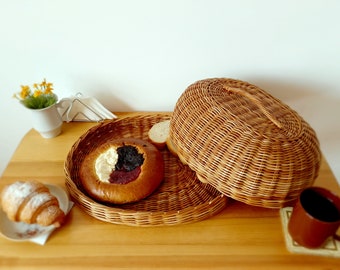 Puede incluir: Una cesta de pan de mimbre con tapa, una bandeja redonda de mimbre con un pastel relleno de crema y mermelada, un croissant y una taza de café sobre una mesa de madera.