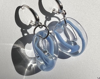 May include: A pair of handmade glass earrings with a light blue swirl design. The earrings are on a white card that reads "GLASS BERRIES" and "handmade glass jewelry". The earrings have silver hoops.