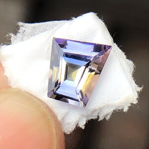 May include: A faceted, purple and clear gemstone with a rectangular shape.