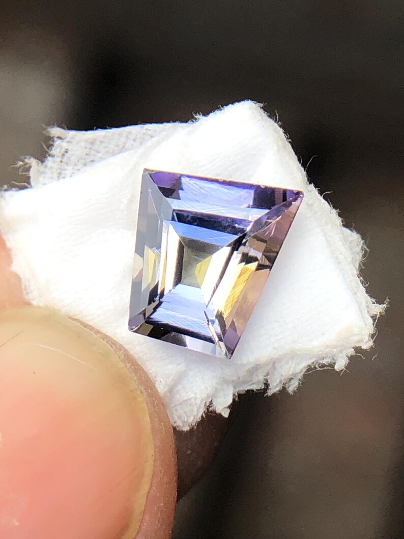 May include: A faceted, purple and clear gemstone with a rectangular shape.