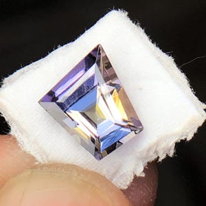 May include: A purple and brown gemstone with a rectangular shape and a faceted cut.