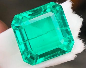 Könnte beinhalten: Ein lebendiger, smaragdgeschliffener Edelstein mit einem satten, grünen Farbton. Der Edelstein ist vor einem weißen Hintergrund platziert, der seine Klarheit und Facetten hervorhebt. Die rechteckige Form und die präzisen Schnitte unterstreichen die Brillanz des Steins.