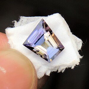 May include: A faceted, rectangular, purple and brown gemstone with a light, almost translucent appearance.