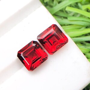 May include: Two red square-shaped gemstones with a faceted cut.