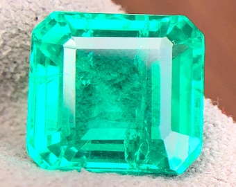 Könnte beinhalten: Ein lebendiger, smaragdgeschliffener Edelstein mit leuchtend grüner Farbe. Der Edelstein hat eine rechteckige Form mit präzise geschliffenen Facetten, die das Licht reflektieren. Der Edelstein ist vor einem neutralen Hintergrund platziert.