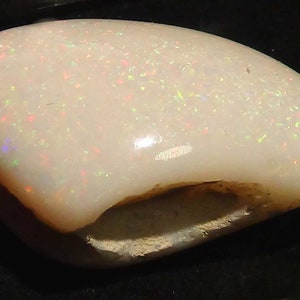 Op de afbeelding: Een witte opaal edelsteen met een ruwe, natuurlijke vorm en een glad, gepolijst oppervlak. De opaal heeft een doorschijnende uitstraling met een vleugje iriserende kleur.
