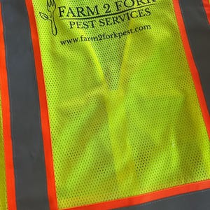 Op de afbeelding: Een neon-geel veiligheidsvest met hoge zichtbaarheid en verticale oranje en grijze reflecterende strepen. De achterkant toont een zwarte afbeelding van een vork gecombineerd met een blad, en de tekst FARM 2 FORK PEST SERVICES en www.farm2forkpest.com.