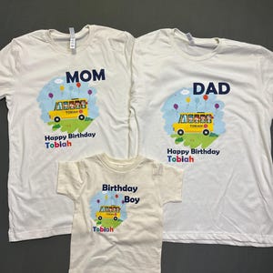 May include: White t-shirts with custom designs for a family. The shirts feature a yellow school bus graphic with the text "Happy Birthday Tobiah". One shirt says "MOM", another says "DAD", and the third says "Birthday Boy".