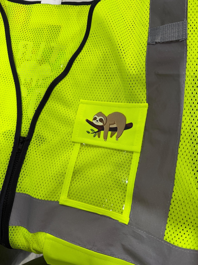 Op de afbeelding: Een neongeel veiligheidsvest met hoge zichtbaarheid van mesh-stof met zwarte randen en reflecterende zilveren verticale strepen. Een klein rechthoekig zakje aan de voorzijde toont een grafische illustratie van een bruine luiaard op een tak.