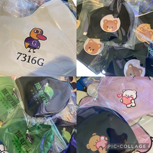 May include: A collection of fabric face masks with various designs. Some masks feature cartoon animals, including a duck, bear, and a creature from the Black Lagoon. Other masks feature text, including "The Reptile Hotel" and "7316G".