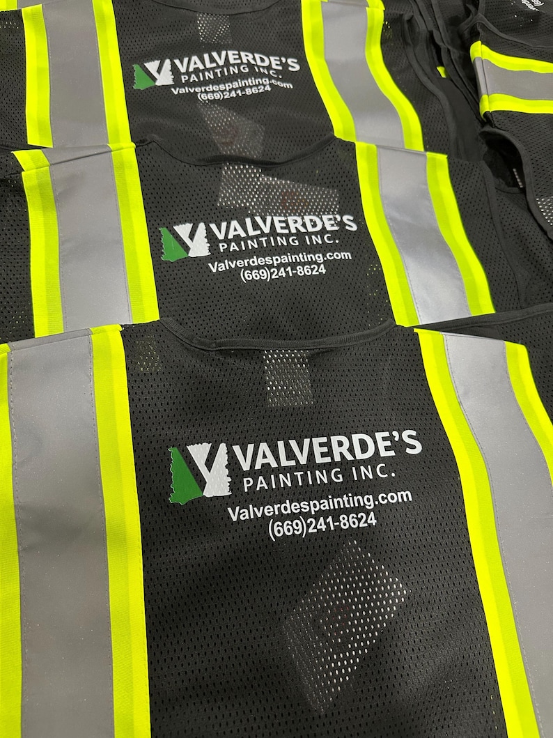Op de afbeelding: Zwarte veiligheidsvesten van mesh met neongele reflecterende verticale strepen. Op de achterkant van elk vest staat het wit-groene logo van Valverde's Painting Inc., de website Valverdespainting.com en het telefoonnummer (669)241-8624.