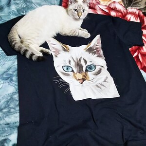 Pu&ograve; includere: Una maglietta nera con una stampa grafica di un gatto bianco. Il gatto ha gli occhi azzurri e un viso con un motivo bianco e marrone. Un gatto bianco con gli occhi azzurri &egrave; sdraiato sopra la maglietta.