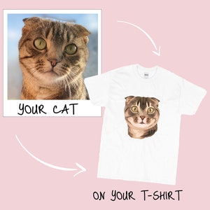 Pu&ograve; includere: Una maglietta bianca con un'illustrazione di un gatto marrone e beige con gli occhi verdi. Il testo "YOUR CAT" &egrave; su una cornice Polaroid bianca sopra il gatto e il testo "ON YOUR T-SHIRT" &egrave; sotto il gatto.