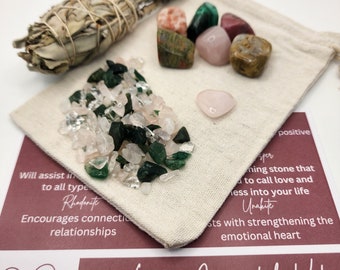 May include: A white cloth bag filled with various crystals, including pink rose quartz, green aventurine, and clear quartz. The bag is sitting on a white surface with a printed card that reads "Love Crystal Kit" and includes descriptions of the crystals.