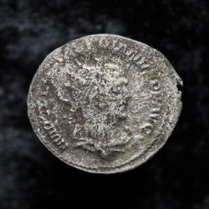 Puede incluir: Una moneda de plata con una superficie desgastada y una imagen en relieve de la cabeza de una persona en un lado. La moneda tiene un borde elevado y algunos de los detalles están desgastados.