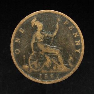May include: A bronze One Penny coin from 1882. The coin features a seated Britannia figure holding a trident and a shield. The words "ONE PENNY" are inscribed around the edge.