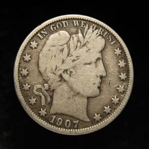 Puede incluir: Una moneda de medio dólar estadounidense de plata con el perfil de un hombre con una corona de laurel. La moneda tiene las palabras "In God We Trust" y "1907" inscritas en ella.