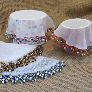 May include: Three white crocheted doilies with colourful beaded trim. The doilies are on a hessian background.