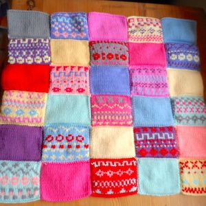 May include: A square knitted blanket composed of a grid of twenty-five individual patches. The patches feature a variety of solid colours including red, pink, blue, yellow, and purple, alongside intricate multi-coloured geometric and floral patterns.