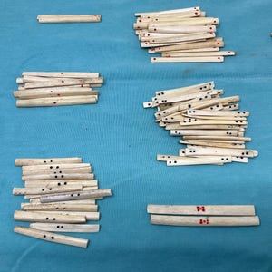 May include: A collection of small, rectangular, off-white wooden pieces with black dots and red markings. The pieces are arranged in several piles on a blue surface. Some pieces have two or three black dots, while others have red markings.