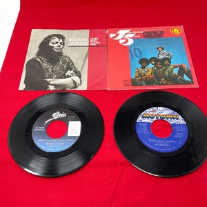 May include: A collection of vintage vinyl records and album covers featuring Michael Jackson and The Jackson 5. The records are black, with labels in blue and white. Album covers are red and white.